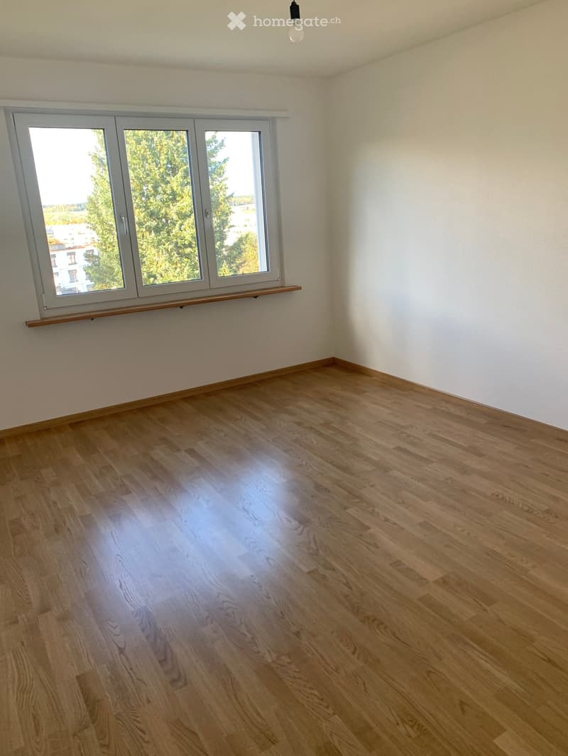 Empty room with wooden flooring, white walls, and large windows with a wooden sill.