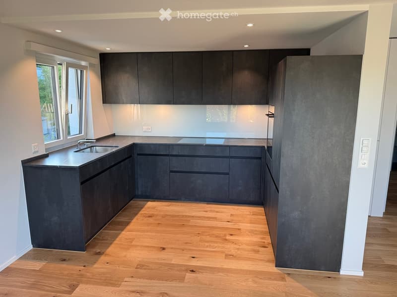 Modern kitchen with dark grey cabinets, a central island, and a wooden floor. Features a sink with a modern faucet and ample cabinet space.