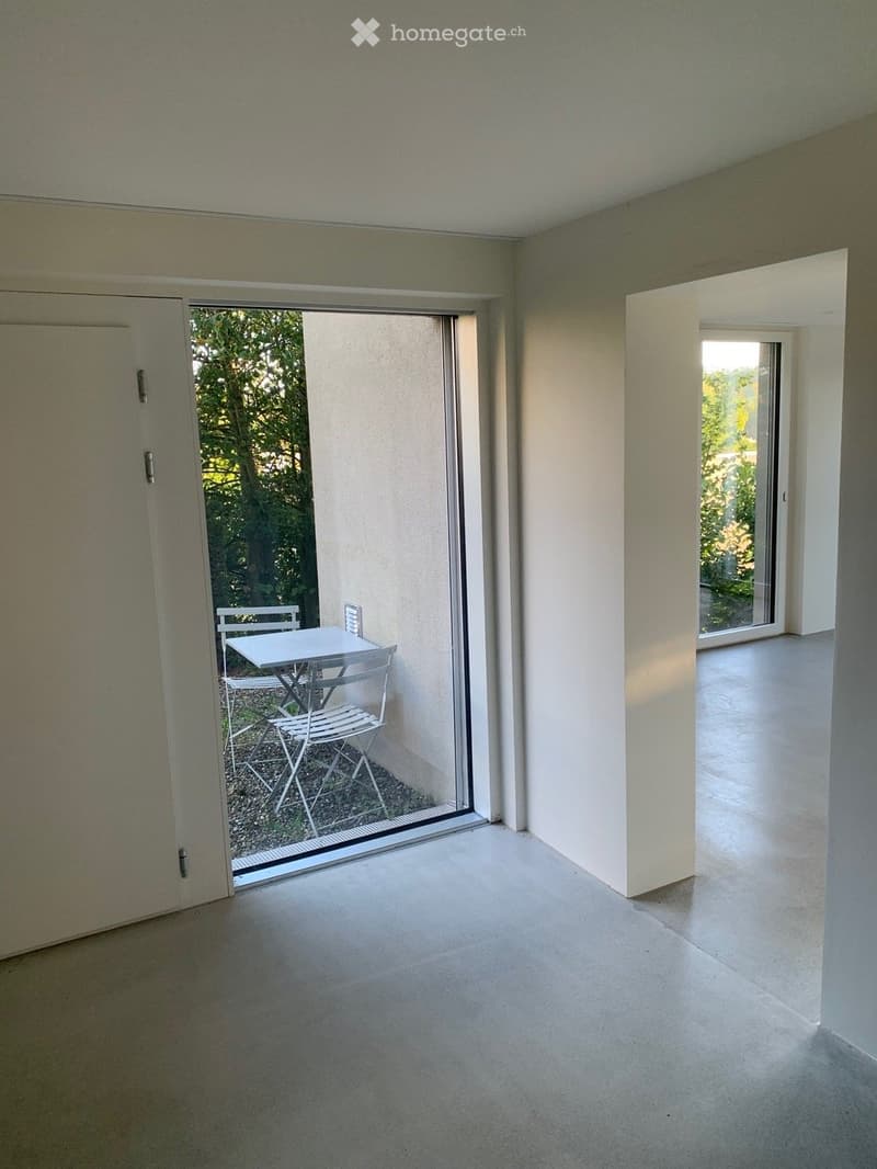 A modern, minimalist room with a large sliding glass door leading to a small outdoor seating area with a table and chairs.