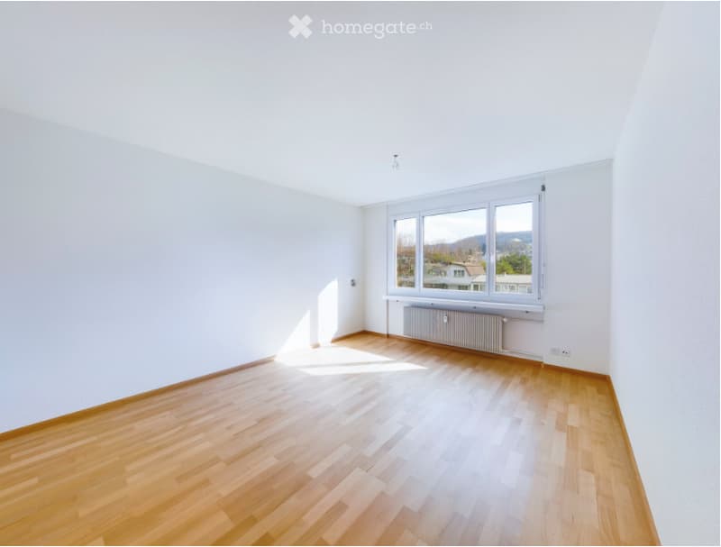Empty room with wooden flooring, white walls, and large windows offering a view of the outside. No furniture or equipment present.
