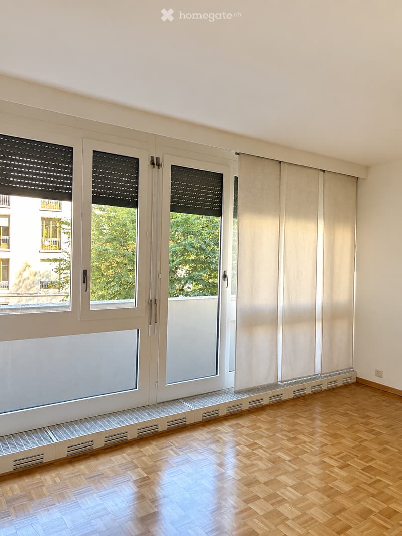 Empty room with wooden flooring, large windows with blinds, and white walls.