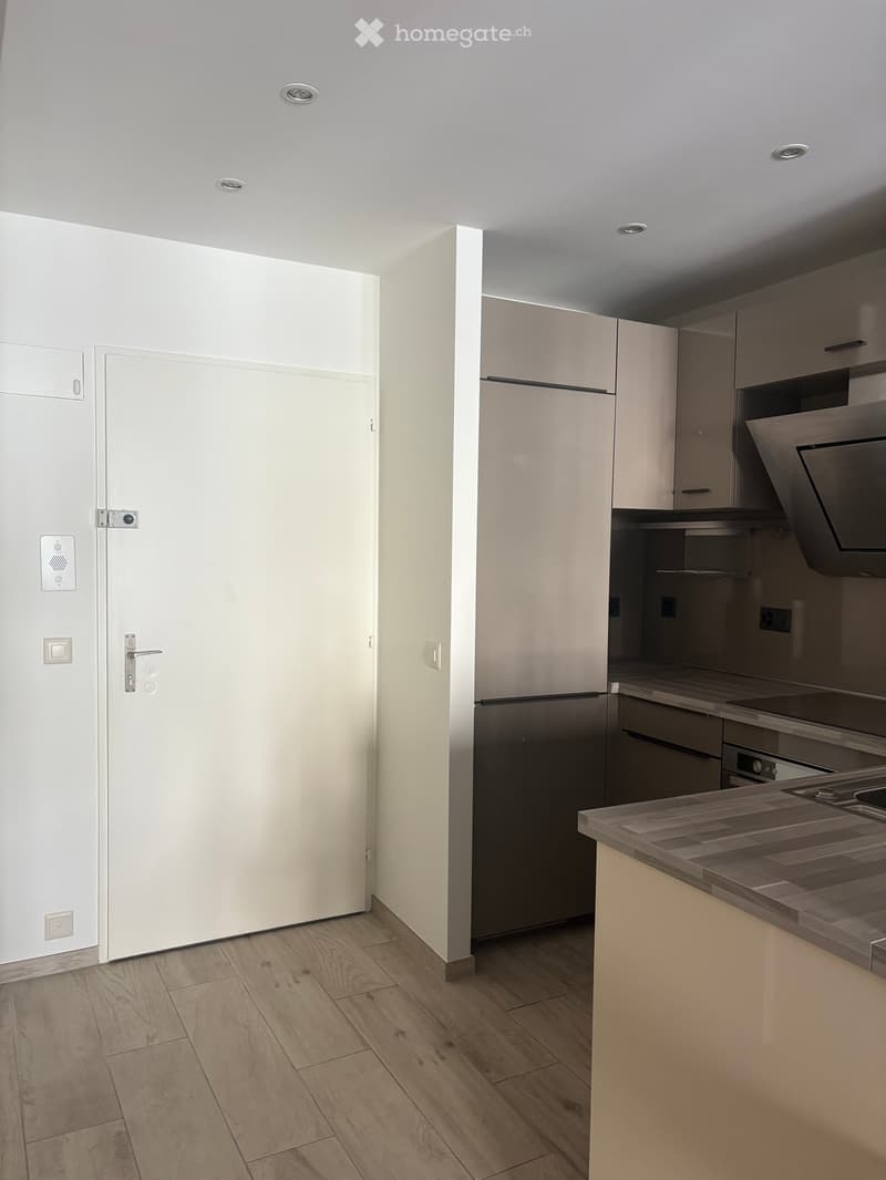 Modern kitchen with light wood flooring, white walls, and grey cabinets. Features a stainless steel refrigerator, oven, and range hood, along with a wooden countertop.