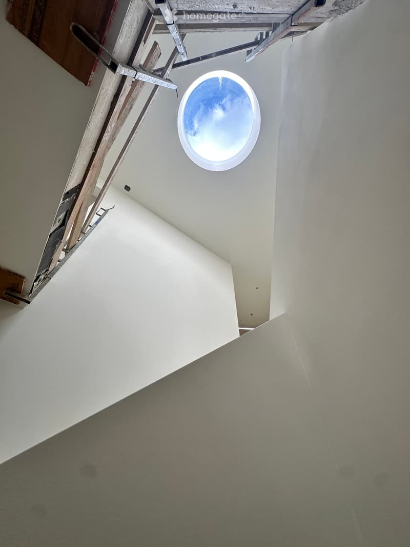 Empty hallway with white walls, carpeted floor, and a circular skylight showing a blue sky.