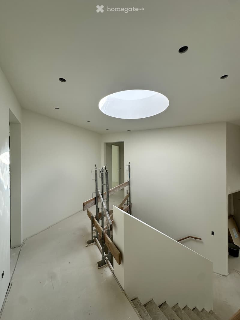 Empty hallway with white walls, a skylight ceiling, and a staircase under construction with wooden railings and metal supports.