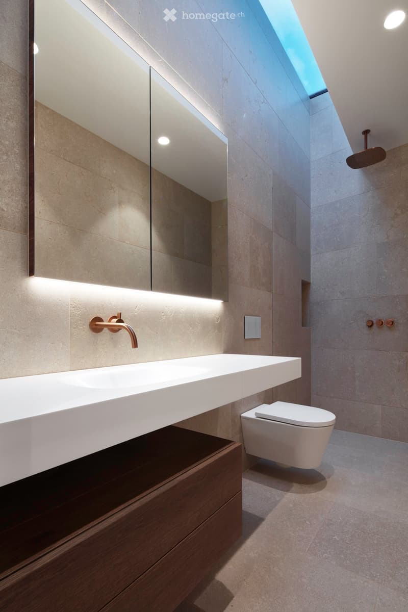 Bathroom with large mirror, white sink, white toilet, modern fittings, skylight, wooden cabinet, tiled wall