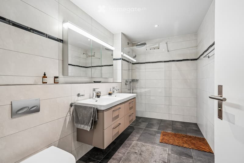 Modern bathroom with a white sink, beige cabinet, large mirror, shower area, and tiled walls and floor.