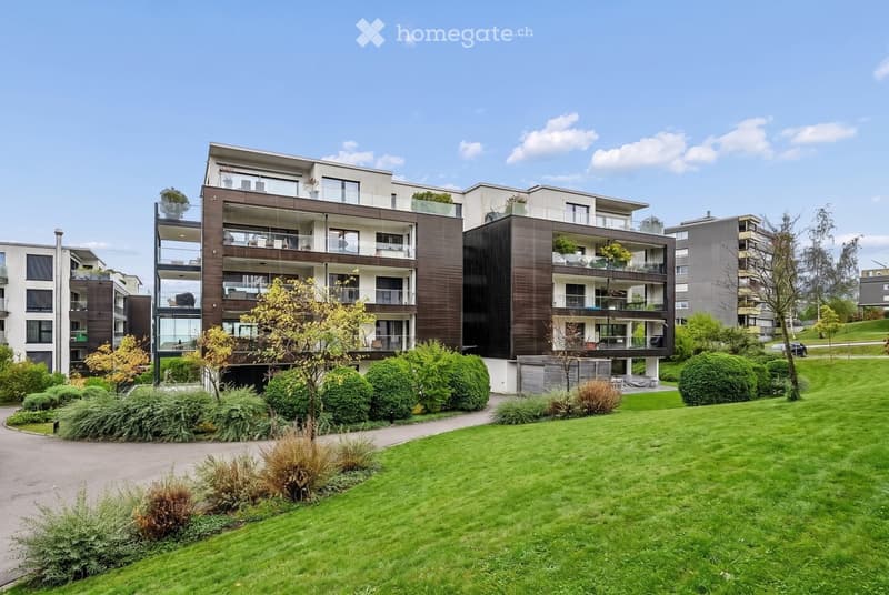 Modern multi-story residential building with balconies, surrounded by well-maintained green lawn and shrubs.