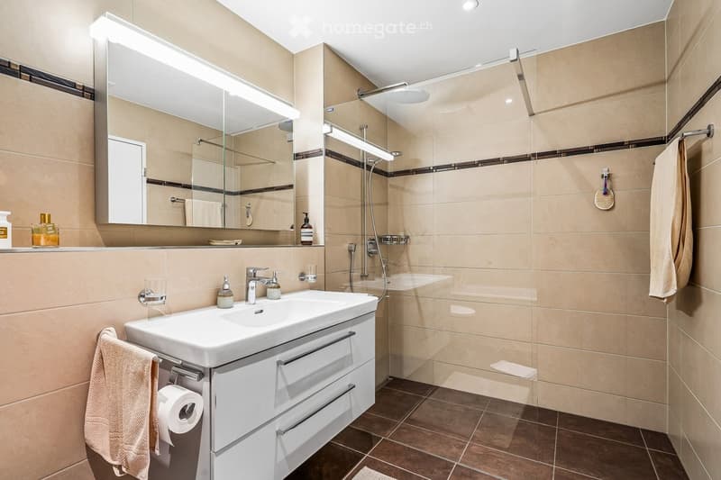 Modern bathroom with a white sink, large mirror, shower area, and neatly arranged towels and toiletries.