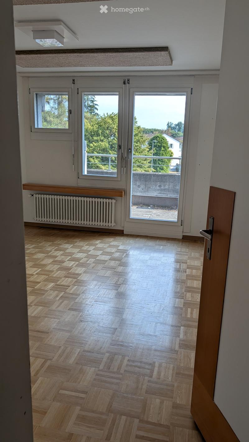 Empty room with wooden herringbone flooring, white walls, large windows, and a radiator. No furniture or equipment present.