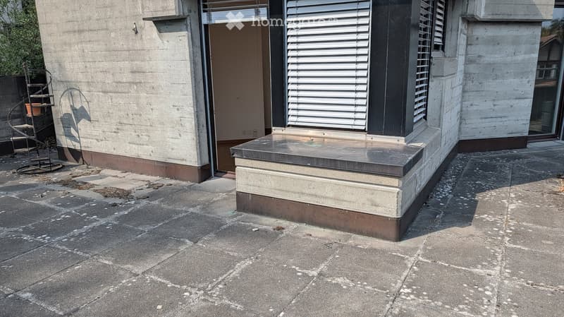 Concrete balcony with a raised edge, metal shutters, and a small metal staircase leading to the ground.