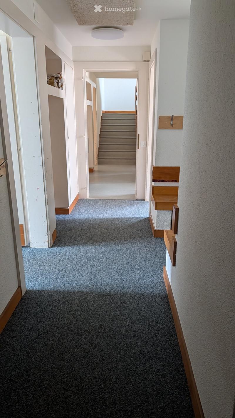 Carpeted hallway with white walls, wooden trim, and a staircase leading upwards.