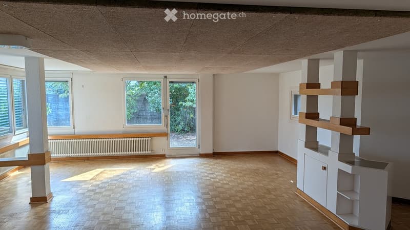 Empty room with wooden flooring, white walls, large windows, and a built-in shelving unit.