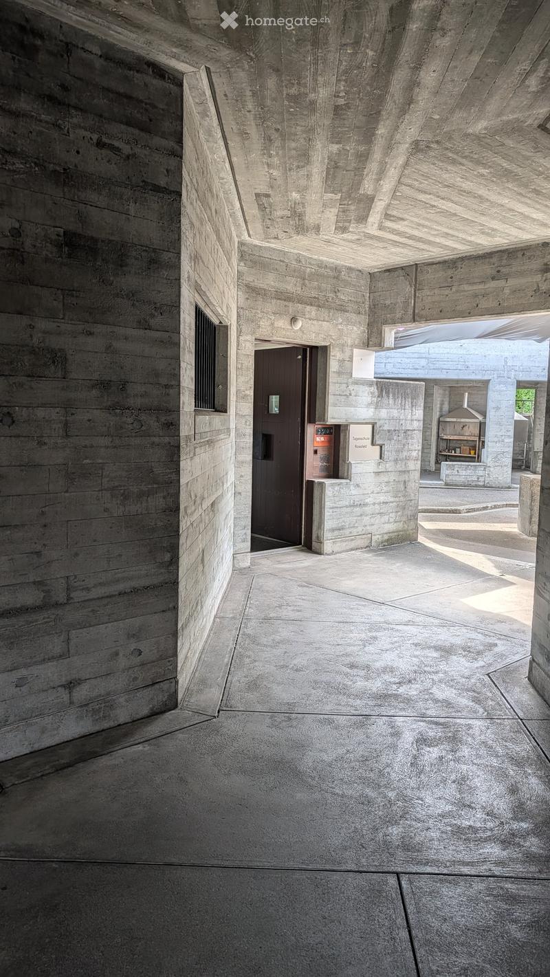 Minimalist concrete corridor with smooth walls, a door, and a small shelf area visible in the background.
