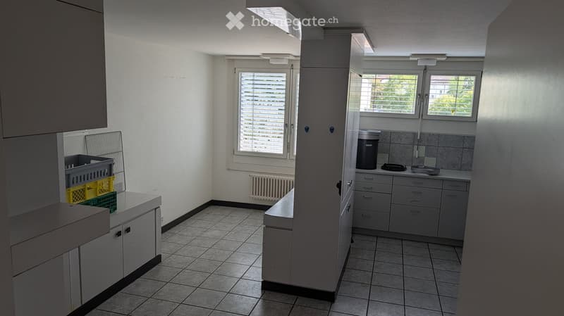Empty kitchen with white cabinets, tiled floor, and windows with blinds. No furniture or appliances are present.