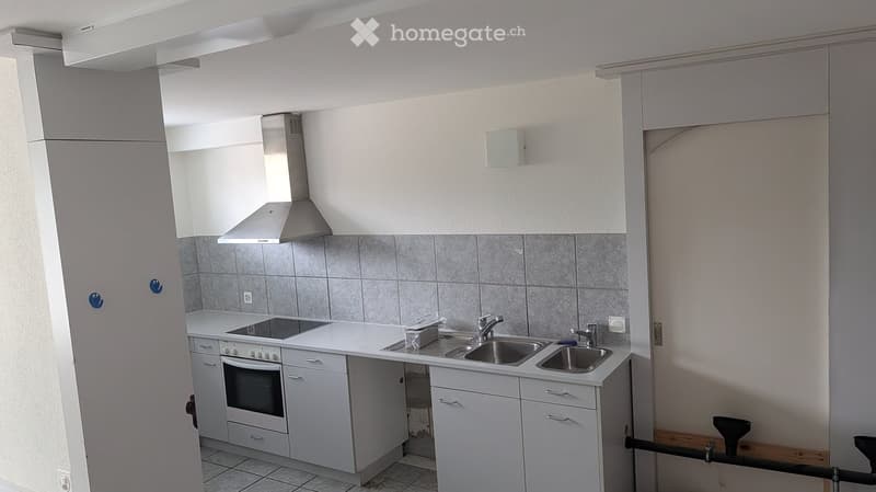 Modern kitchen with white cabinets, stainless steel sink, oven, and range hood. Grey tiled backsplash and tiled floor.