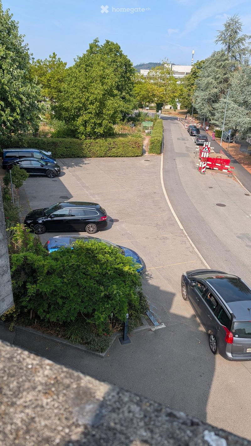 Parking area with several cars parked, surrounded by greenery and a road with traffic barriers.
