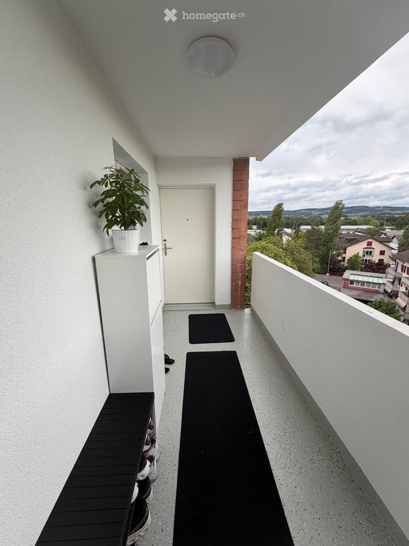 Balcony / Terrace. Modern balcony with grey concrete floor, white walls, potted plant, black runner, and black shoe rack.