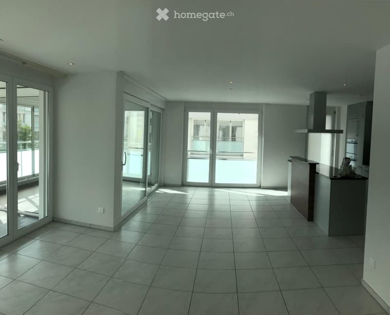 Empty room with tiled floor, large glass sliding doors, and a small kitchen counter with cabinets.