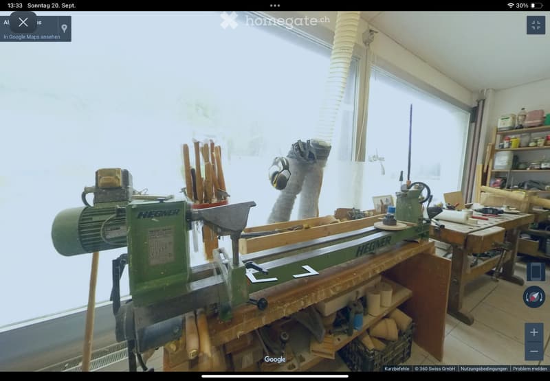 Well-lit workshop with a lathe machine, workbench, shelves filled with tools, and various wooden materials.