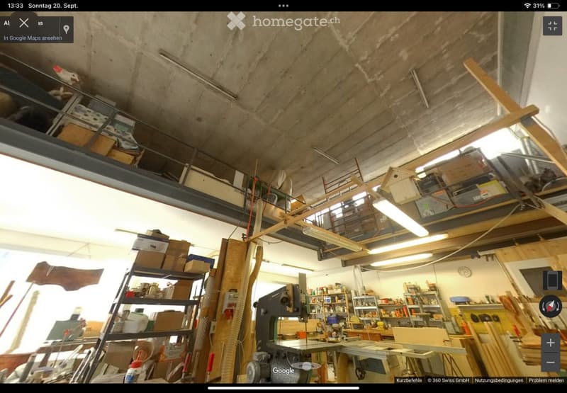 A spacious workshop with exposed concrete ceiling, various tools, workbenches, shelves filled with supplies, and wooden materials.