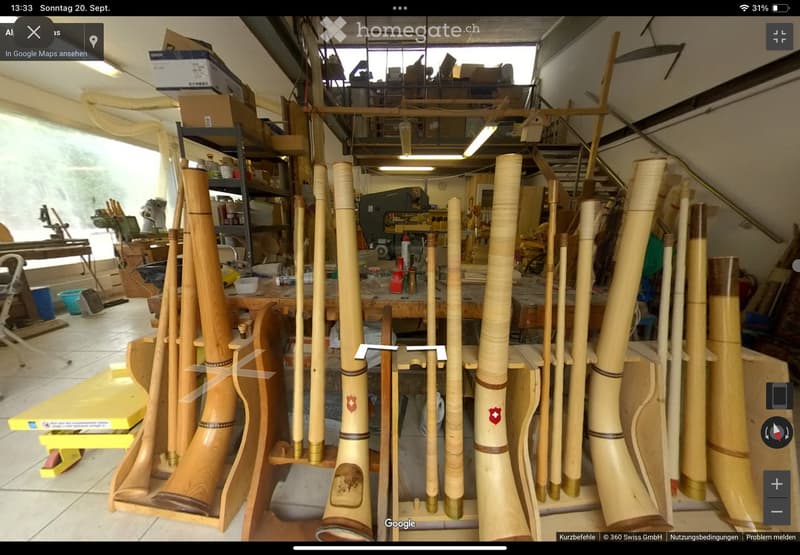Workshop with large wooden instruments displayed, workbench, shelves, and various tools.