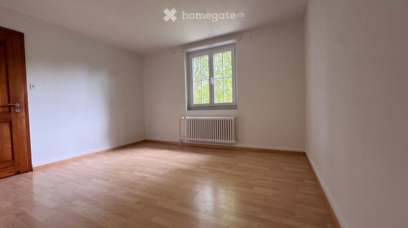 Empty room with light pink walls, wooden floor, a window with white frame, and a radiator below it.