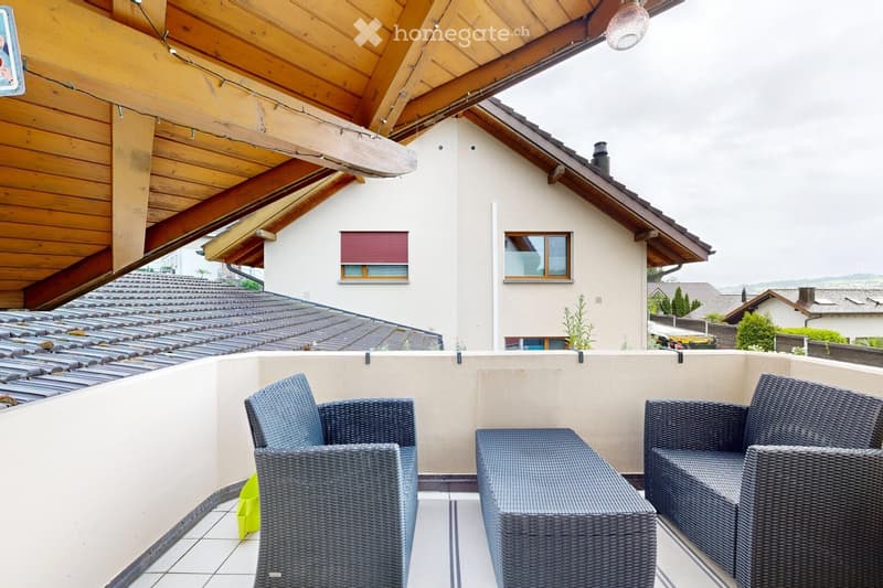 Balcony with wicker chairs, a small table, and a view of the roof and neighboring houses.