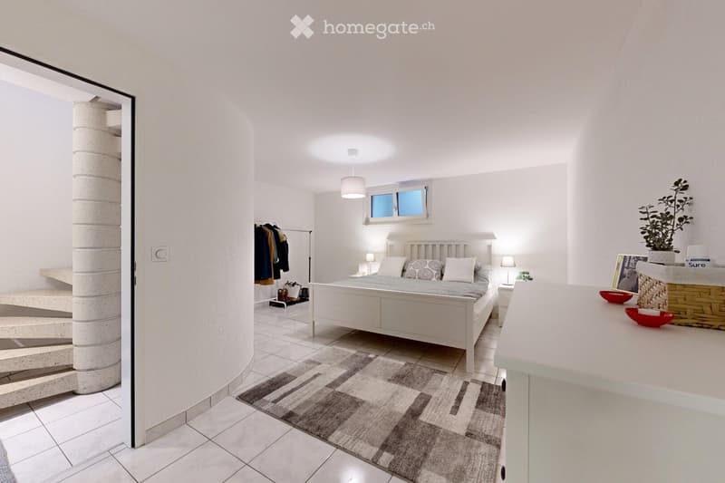 Modern bedroom with a white bed, nightstands, lamps, a patterned rug, and a small seating area with a plant and picture frame.