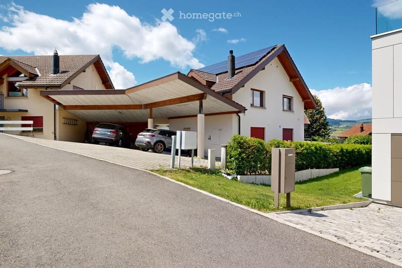Two-story house with a covered driveway, two parked cars, solar panels on the roof, and a well-maintained garden with hedges.