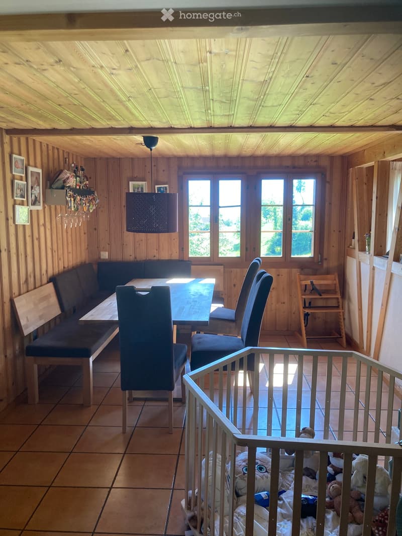 Cozy wooden-paneled room with a dining area featuring a long bench, table, and chairs, along with a hanging lamp and picture frames on the wall.