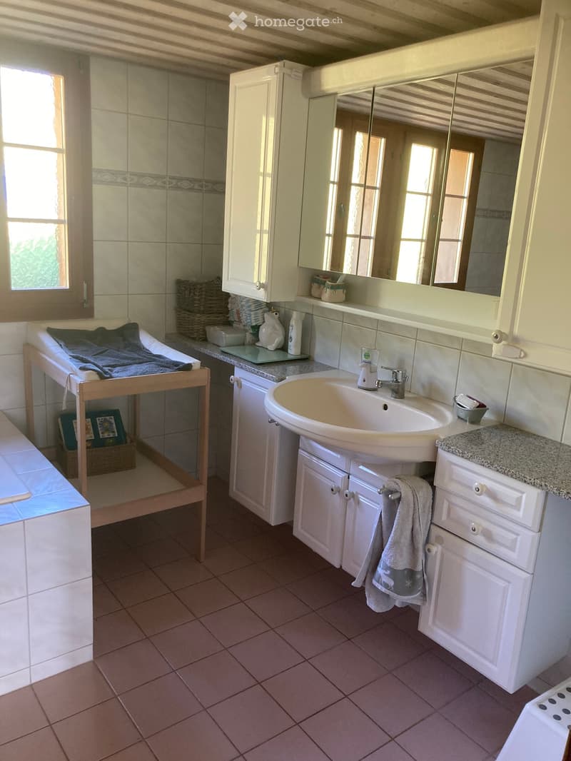 Bathroom with a sink, mirror, white cabinets, tiled walls, and a towel hanging on a rack.