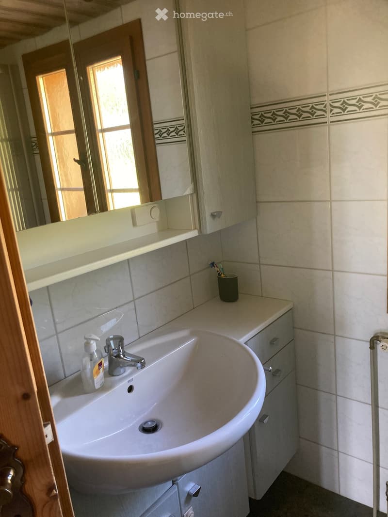 Modern bathroom with a white sink, chrome faucet, mirror, and a toothbrush holder on the counter. The walls are tiled with a decorative border near the top.