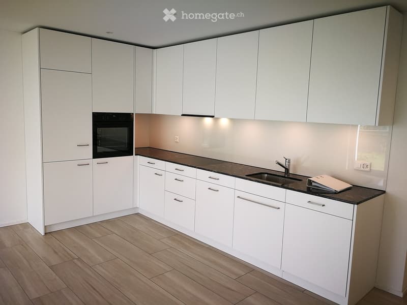 Modern kitchen with white cabinets, dark countertops, and a sink with a faucet. An oven is integrated into the cabinetry.