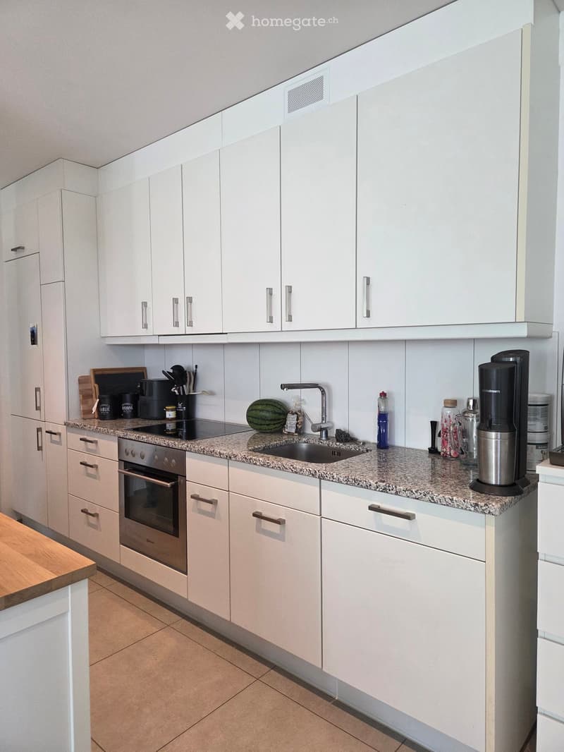 Modern kitchen with white cabinets, granite countertop, built-in oven, sink, and various appliances.