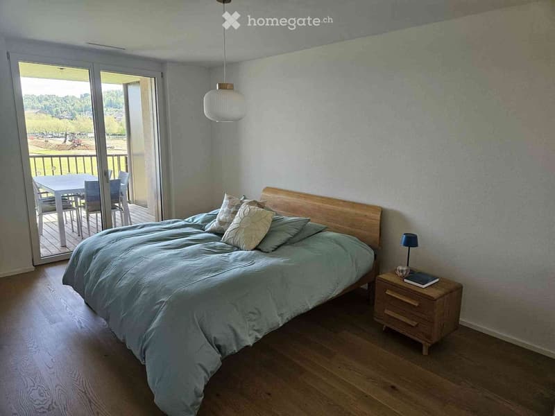 Cozy bedroom with a large bed, nightstand, and a table and chairs near a sliding glass door leading to a balcony.