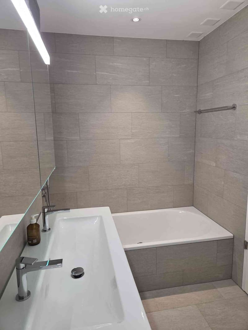 Modern bathroom with a large bathtub, double sink, and a handrail for accessibility.