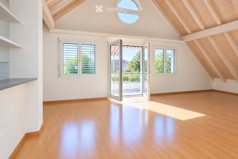 Bright, empty room with wooden flooring, white walls, and large windows, including a skylight and sliding glass doors leading to a balcony.