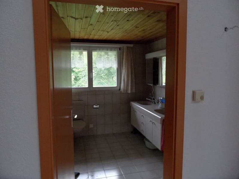 Bathroom with a sink, toilet, and cabinet, featuring tiled walls and floor, and a window with curtains.