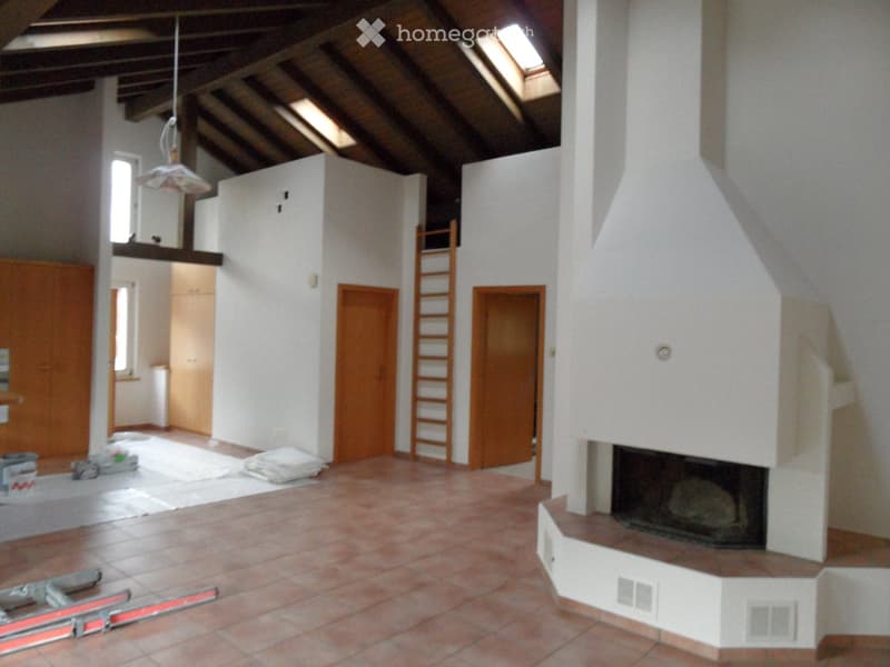Empty room with exposed wooden beams, fireplace, wooden doors, and a ladder leading to an upper level.