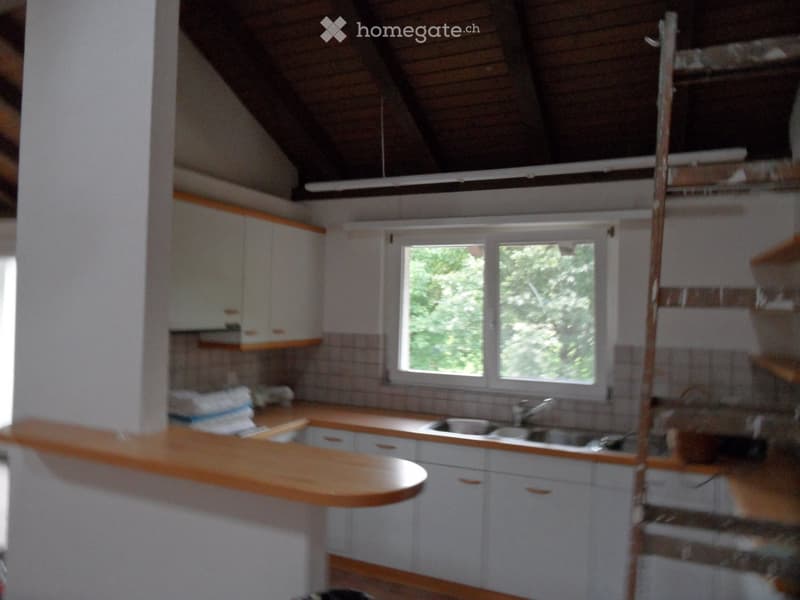 Bright kitchen with white cabinets, wooden countertop, and a double sink under a large window with a view of greenery.