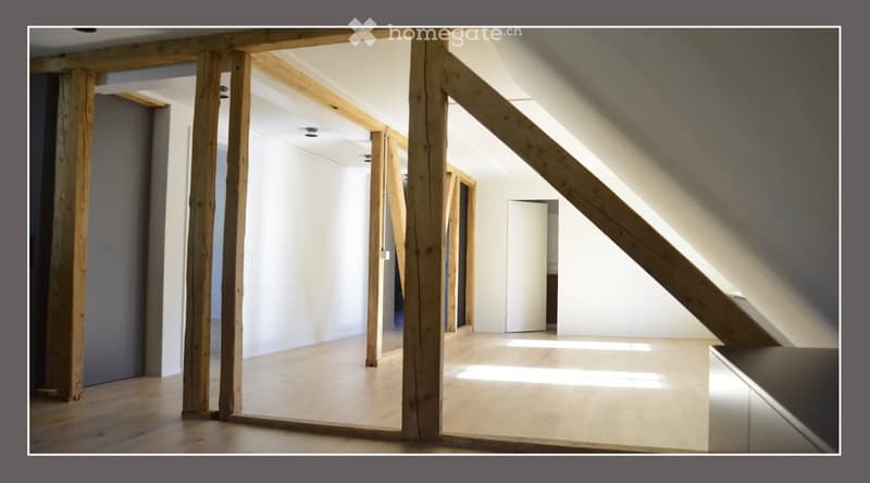Empty room with exposed wooden beams, white walls, and a wooden floor. No furniture or equipment is present.
