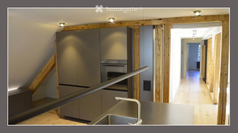 Modern kitchen with stainless steel sink, faucet, built-in oven, and grey cabinets. Wooden flooring and recessed lighting.