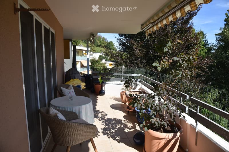 Balcony with tiled floor, wicker chairs, small round table, potted plants, and outdoor furniture.