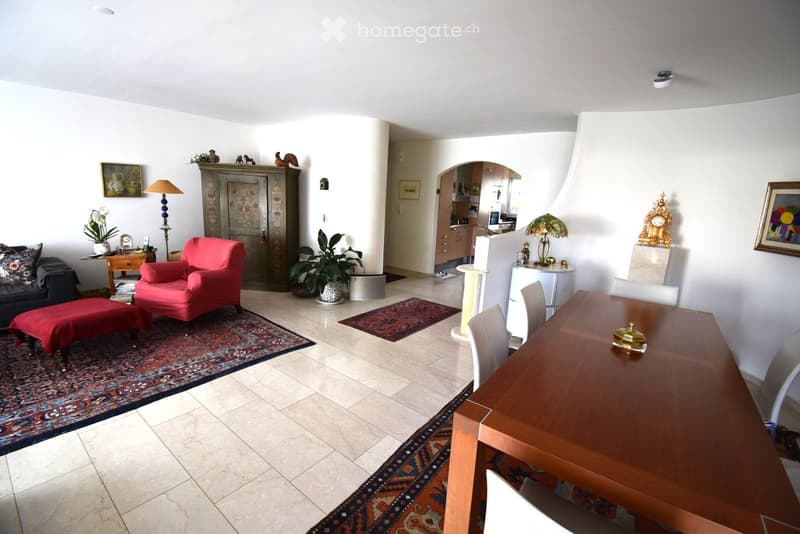 A well-furnished living and dining area with a sofa, red armchair, wooden dining table, and various decorative items including lamps, plants, and a cat tree.