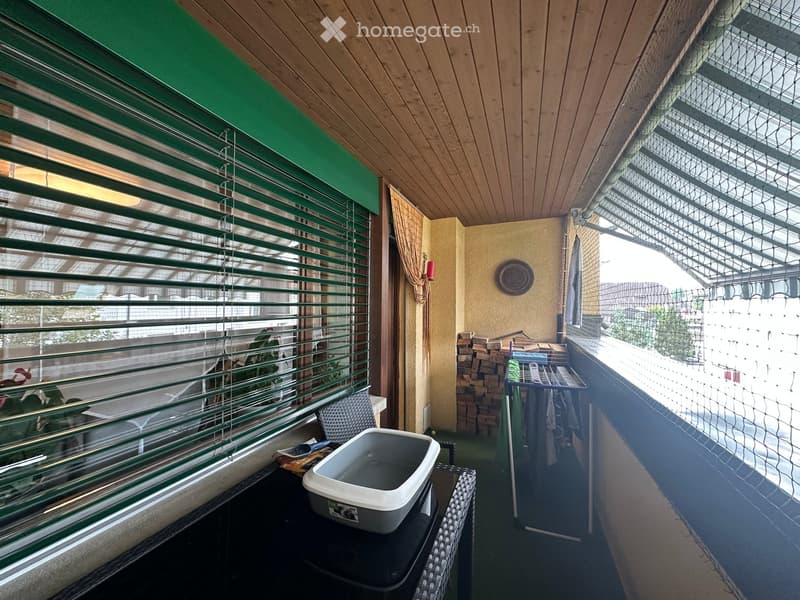 Balcony with wooden ceiling, green blinds, small table with a pet bowl, chair, and a drying rack with clothes.