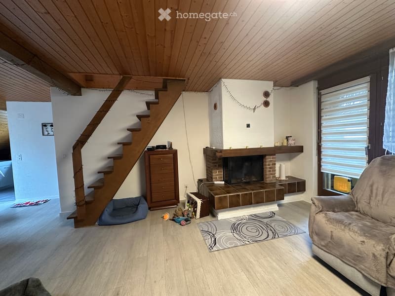 Living room with wooden staircase, fireplace, sofa, pet bed, and wicker basket on the floor.