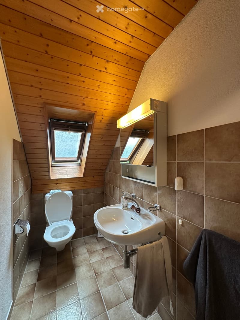 Cozy attic bathroom with wooden walls, tiled floor, toilet, sink, mirror, and towel.