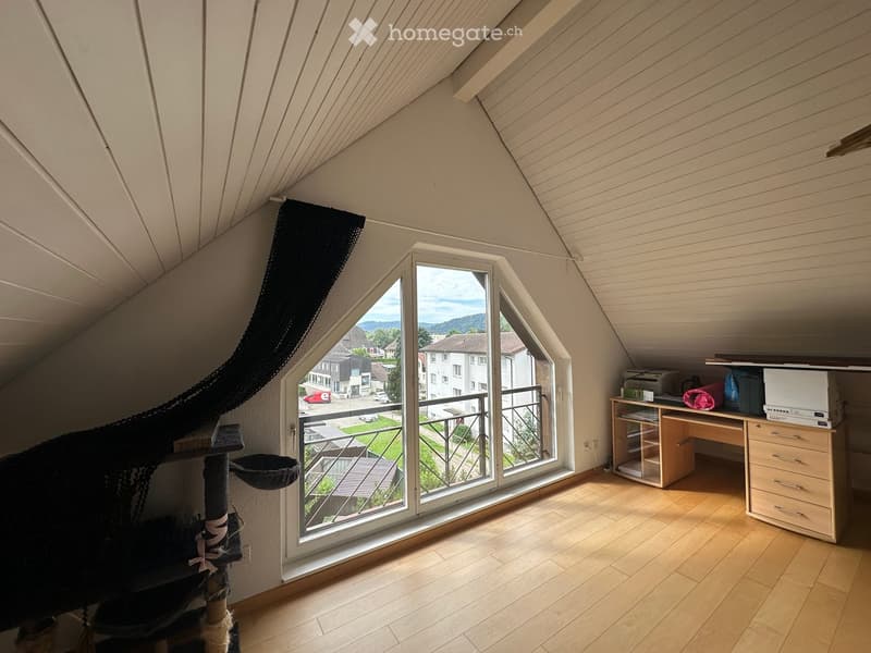 Bright attic room with wooden flooring, large window offering a view, cat tree, desk with printer, and drawer unit.