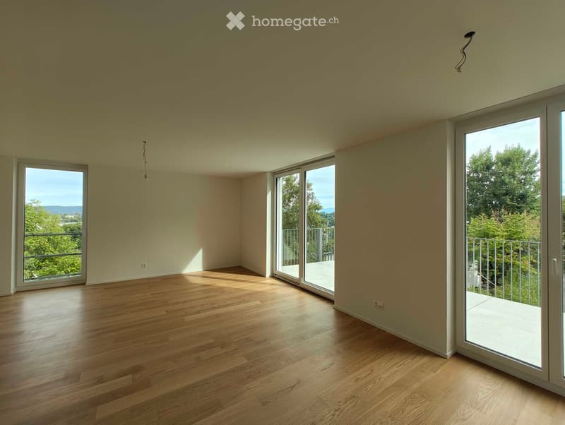 Empty room with wooden flooring, large windows, and sliding glass doors leading to a balcony.