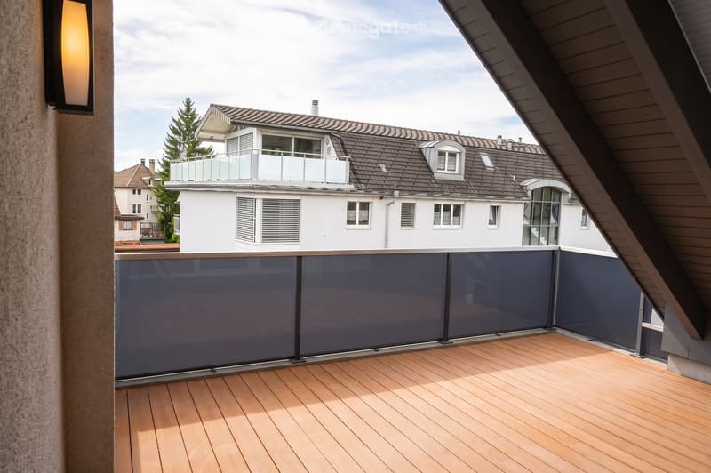 Wooden deck with dark blue glass railing, overlooking a residential area with houses and trees.